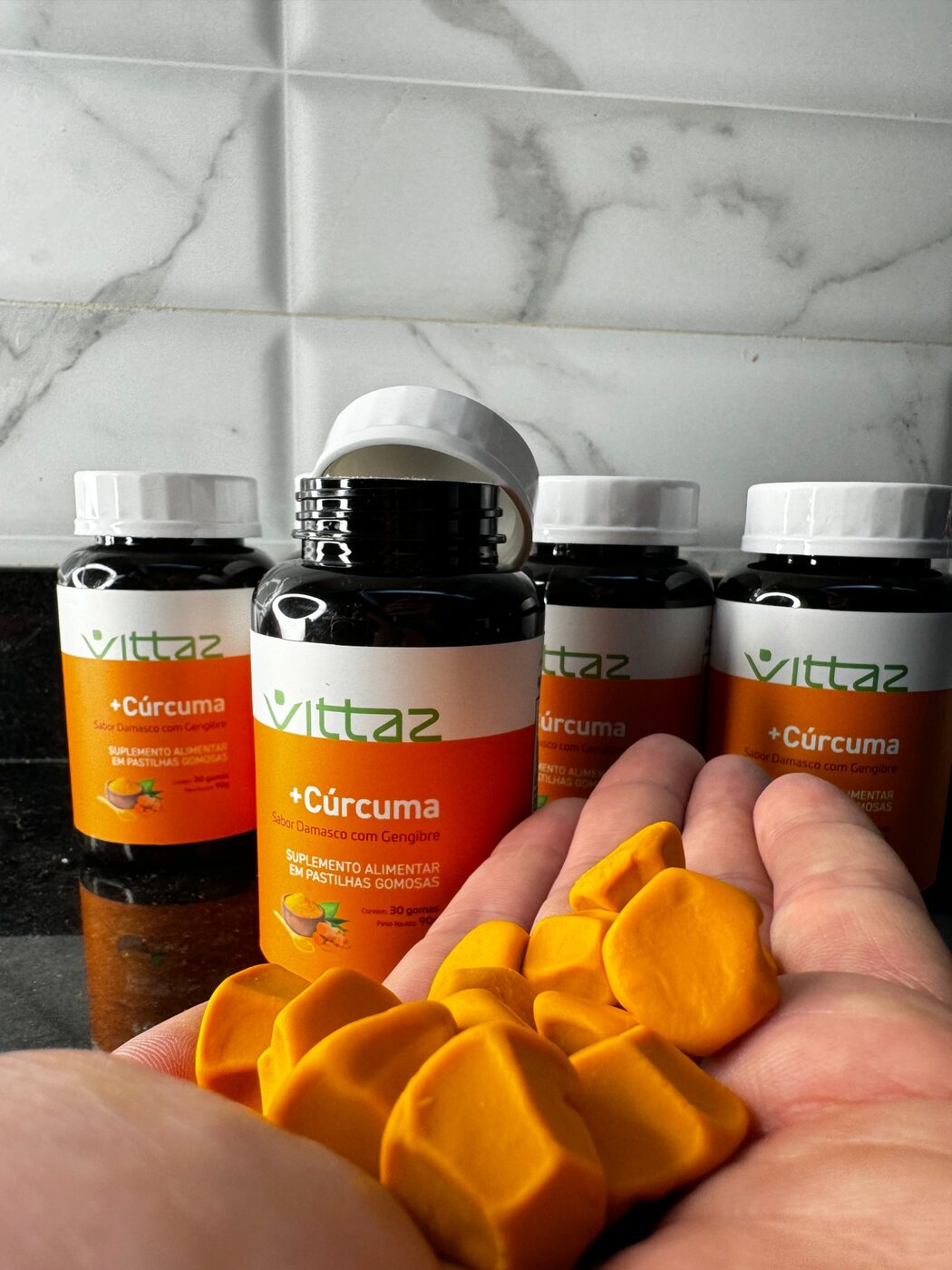 Pastilhas gomosas de cúrcuma Vittaz na mão com os frascos ao fundo